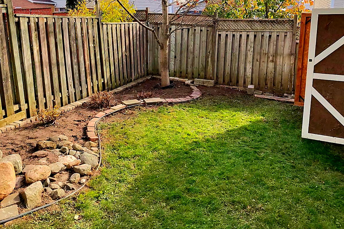The same back corner after a Northline backyard cleanup, lawn clear and the rock garden and bed edge visible again
