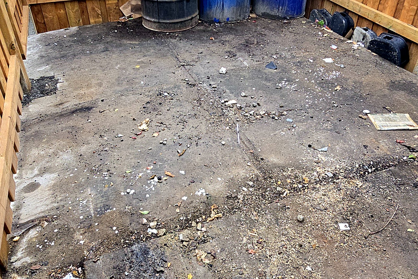 A fenced dumpster enclosure at a commercial property with litter across the ground