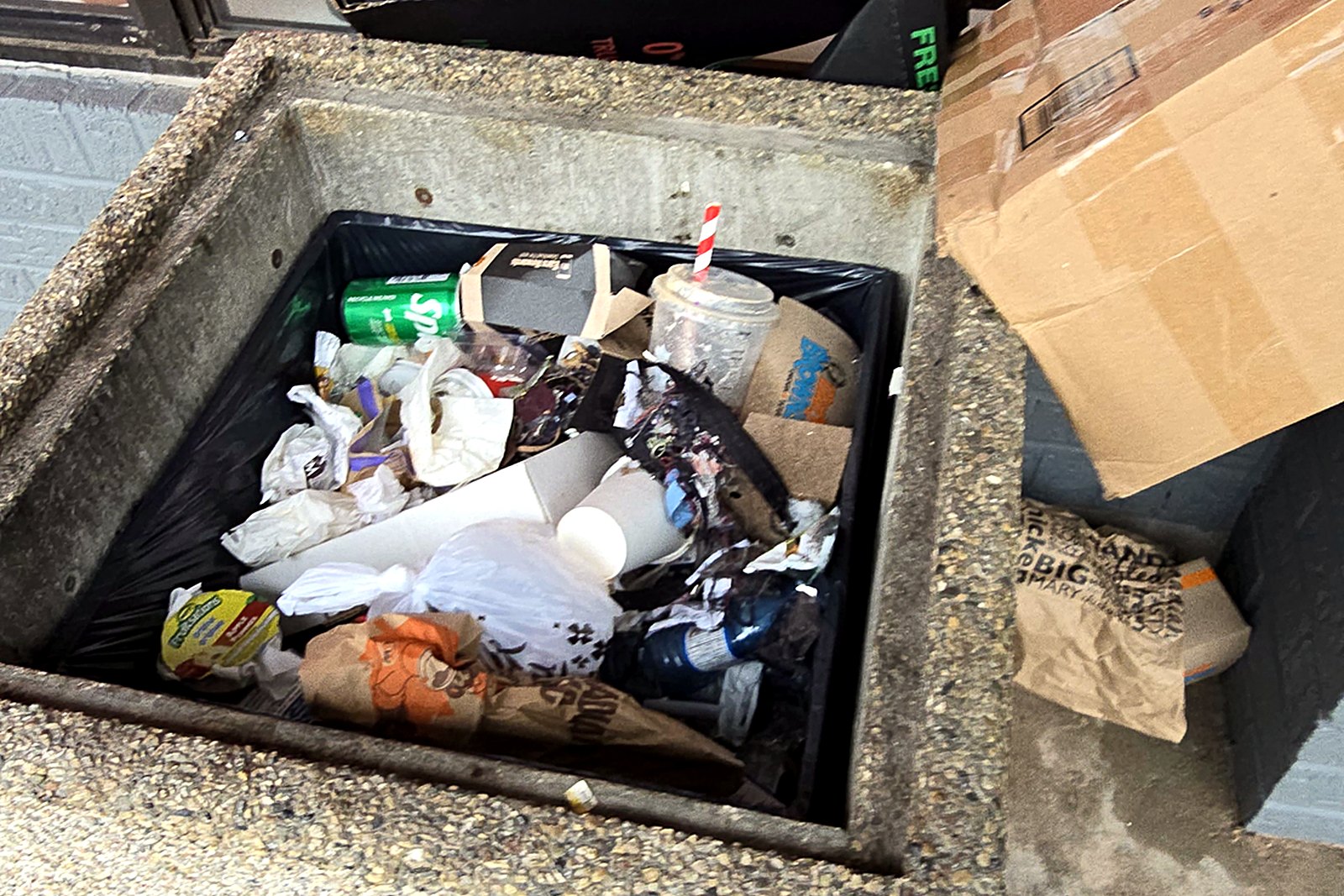 An overflowing storefront garbage receptacle at a commercial property