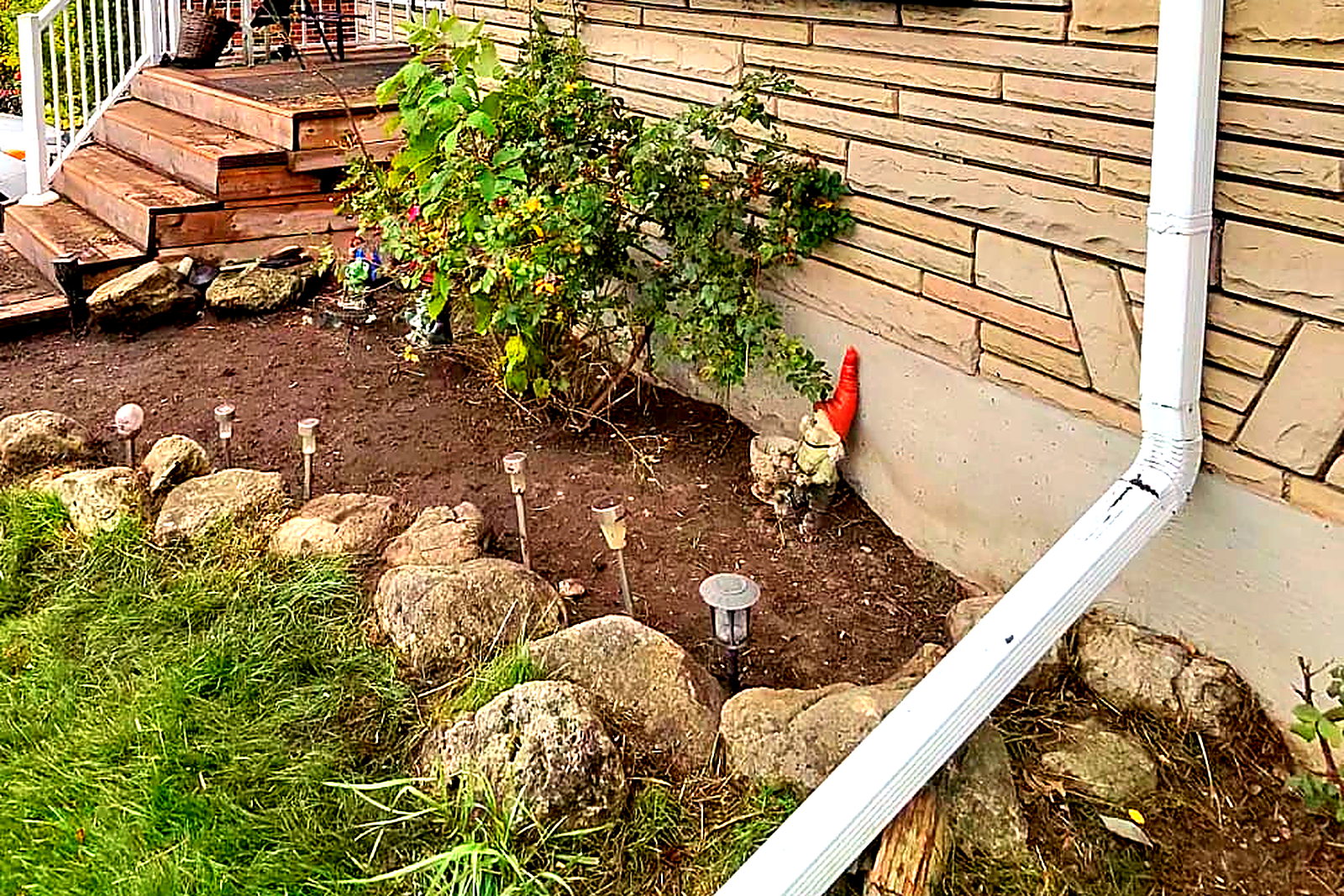 A finished front entry bed edged with stone, cleared to clean soil beside a cedar deck